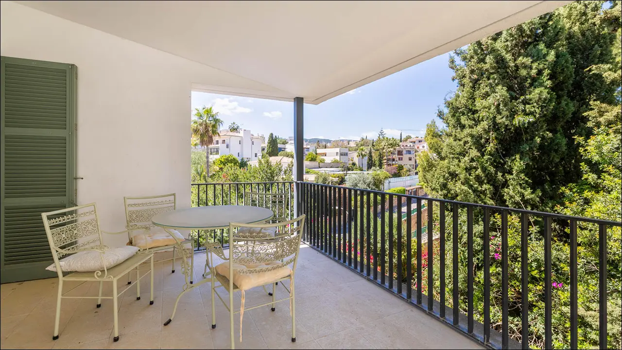 Spacious covered terrace with elegant outdoor dining area, overlooking lush gardens and neighborhood views in a sunny Mallorca