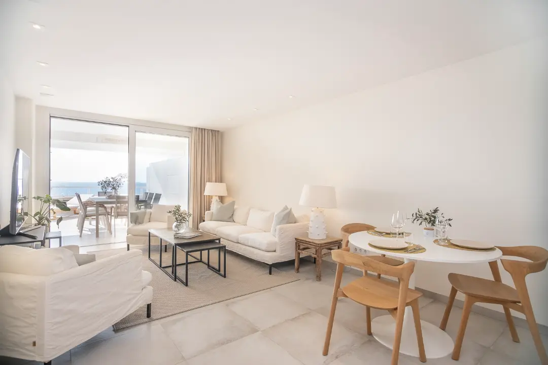 Bright open-plan living and dining area with modern decor and sea view terrace in Puerto Portals apartment for sale.
