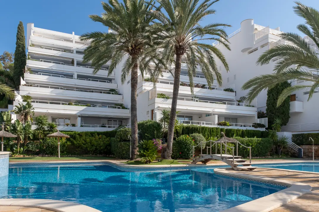Puerto Portals apartment complex with landscaped gardens, palm trees, and community swimming pool in Mallorca.